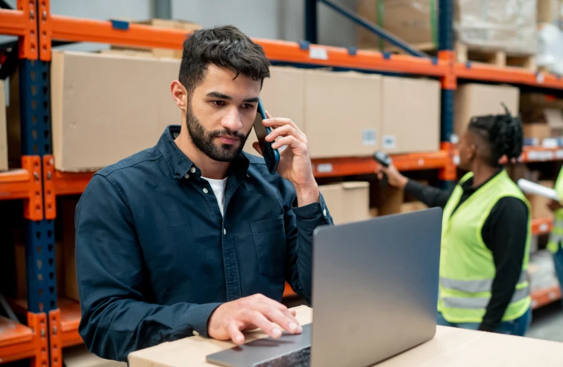 Man in a warehouse talking on the phone and working on a laptop